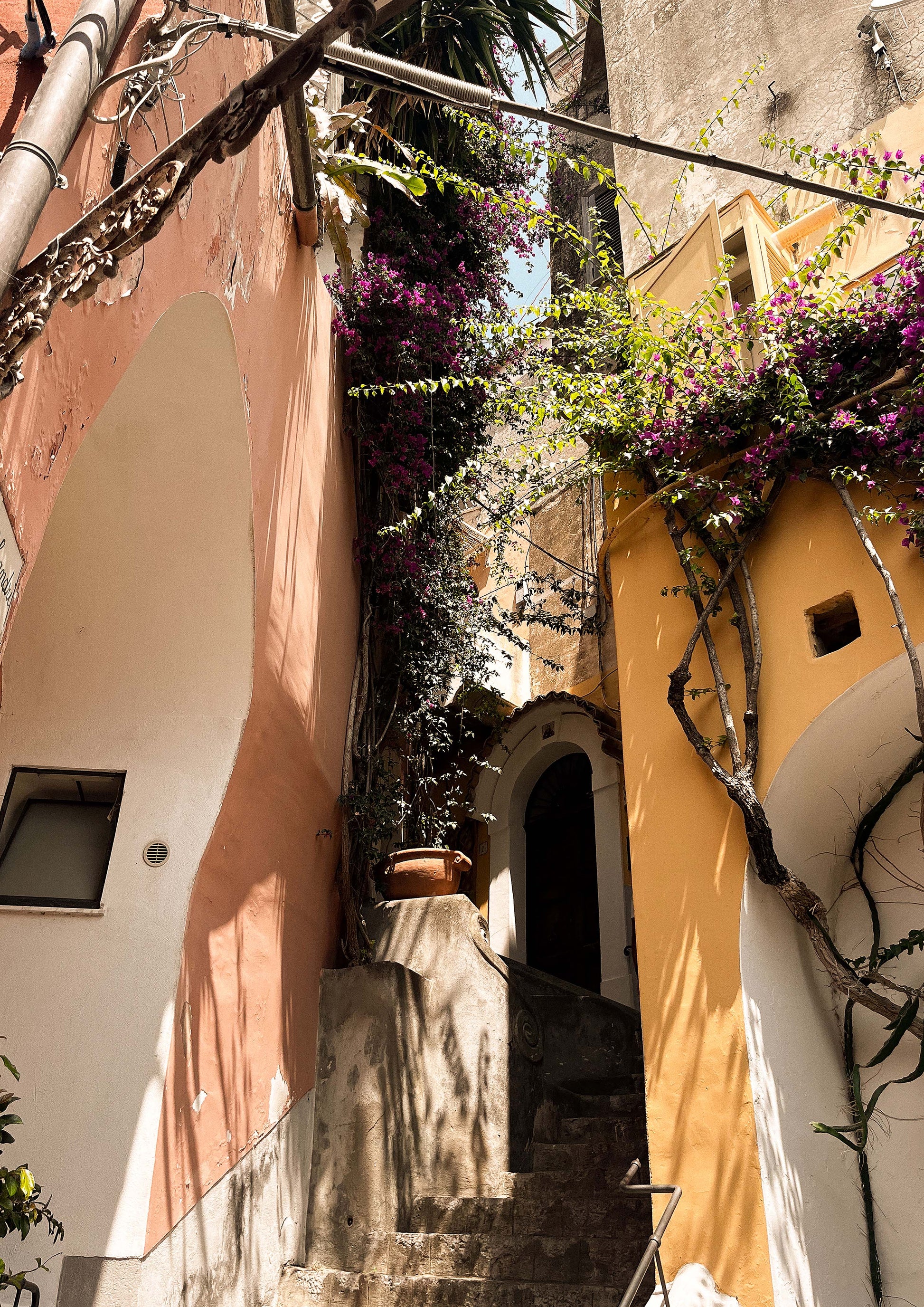 Fine art print titled “Le Strade di Positano,” featuring a sunlit alleyway winding through pastel buildings and bougainvillea in the heart of the Amalfi Coast. This image captures the charm and vibrancy of southern Italy—ideal for coastal, Mediterranean, or wanderlust-inspired interiors.