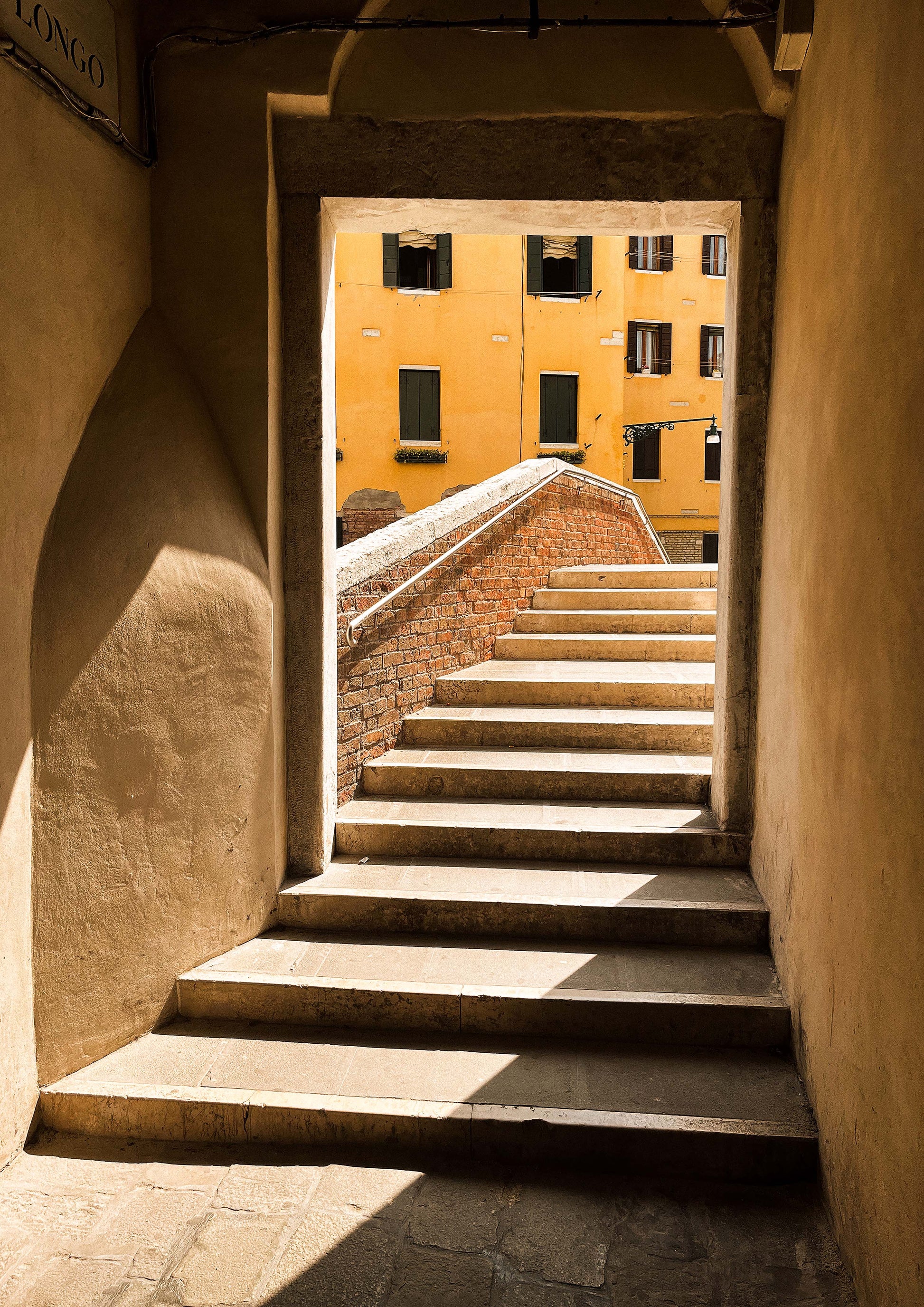 Fine art photograph titled “Le Scale di Venezia,” featuring a winding Venetian staircase bathed in soft natural light and flanked by weathered stone walls. This image evokes the mystery and elegance of historic Venice—ideal for classic, romantic, or travel-inspired interior styling.