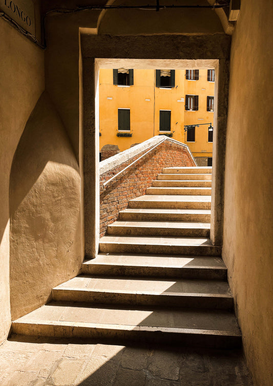Fine art photograph titled “Le Scale di Venezia,” featuring a winding Venetian staircase bathed in soft natural light and flanked by weathered stone walls. This image evokes the mystery and elegance of historic Venice—ideal for classic, romantic, or travel-inspired interior styling.